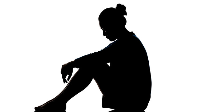 Silhouette of a sad woman sitting alone in darkness feeling depressed or anxious isolated on white background