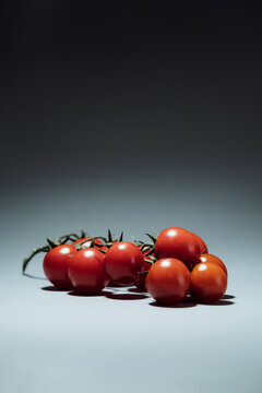 Fresh red cherry tomatoes on a vine against a grey background