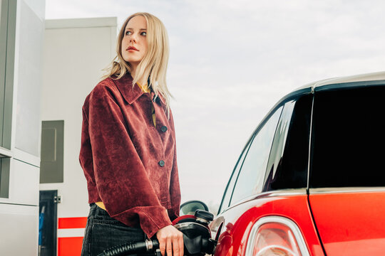 Woman refueling car at gas station with an anxious expression