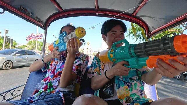 Young Couple Celebrating Songkran Festival with Water Guns in a Tuk Tuk