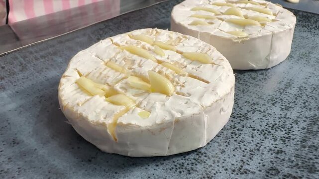 Preparing camembert cheese for baking with garlic, scored top, cloves inserted, ready for oven warmth.