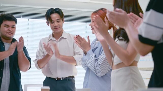 Asian business team clapping hands and smiling after a successful meeting. Celebrating success and teamwork in a modern, bright office conference room.