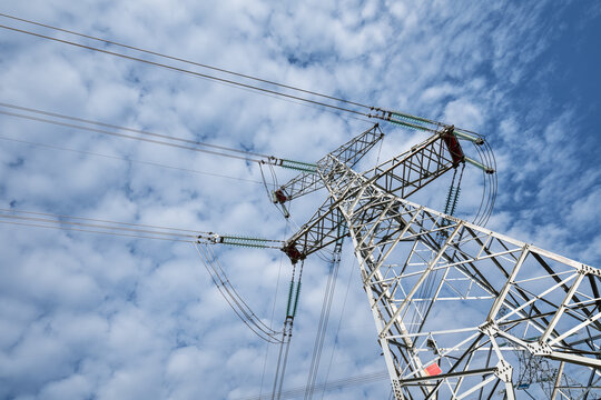 High-Voltage Transmission Tower with Insulators and Power Lines Against a Cloudy Blue Sky