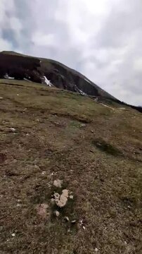 Hyperlapse dinamico di un paesaggio montano con pendii rocciosi, prati verdi e chiazze di neve residua sotto un cielo parzialmente nuvoloso