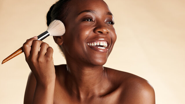 Happy, makeup and black woman with brush for beauty, blush or highlighter with glow. Smile, self care and female person with cosmetic tool and foundation for face cosmetology by studio background.