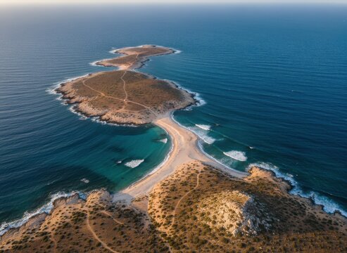 Aerial view of a sandy tombolo connecting a rocky island to the mainland coast