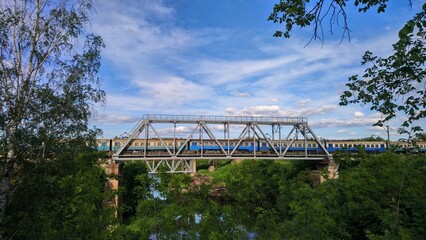 Fototapeta premium Electric passenger train crossing a steel truss bridge over Uzh River in Korosten