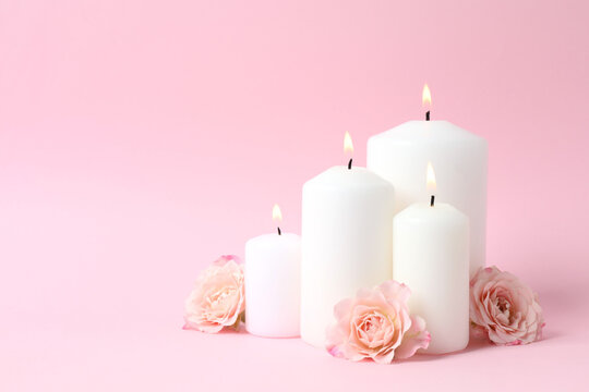 Burning candles with pikk roses on pastel background, space for text