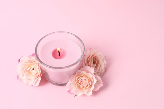 Burning candle with pikk roses on pastel background, space for text