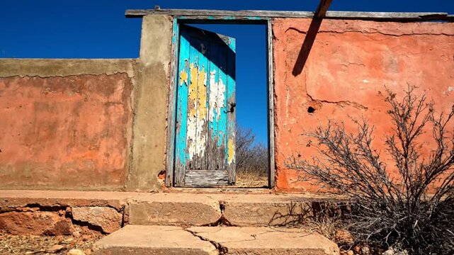 Weathered wooden door in sunlit doorway set within an aged adobe structure against blue sky