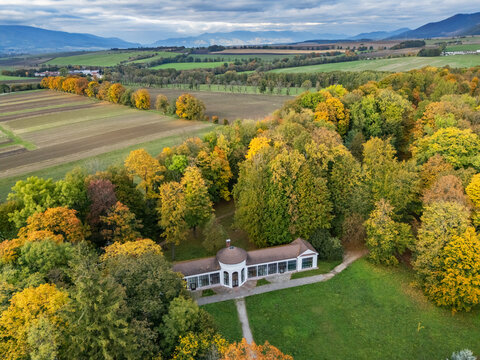 Aerial view of the elegant Mosovce Manor House, its classical architecture nestled amidst a vibrant tapestry of fiery autumn foliage, Mosovce, Zilina Region, Slovakia.