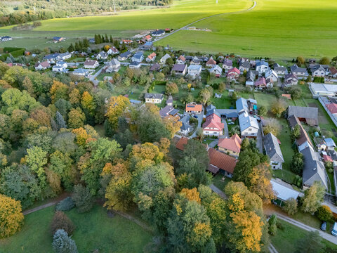 Aerial view of a picturesque village with homes enveloped by a vibrant autumn forest, its foliage green and gold, Mosovce, Zilina Region, Slovakia.