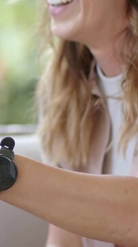 Vertical video: Framing woman in white top turning wrist and talking in lounge showing black device