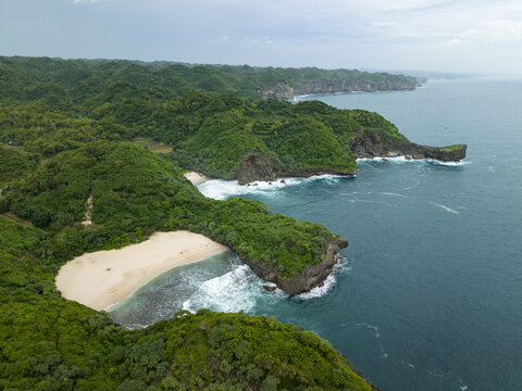 Aerial view of the lush green coastline meeting the turquoise sea at Sedahan Beach, a hidden gem, Gunungkidul Regency, Special Region of Yogyakarta, Indonesia.