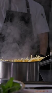 Close-up of pasta being placed into a pot of boiling water by a cook. Cooking process and professional kitchen preparation