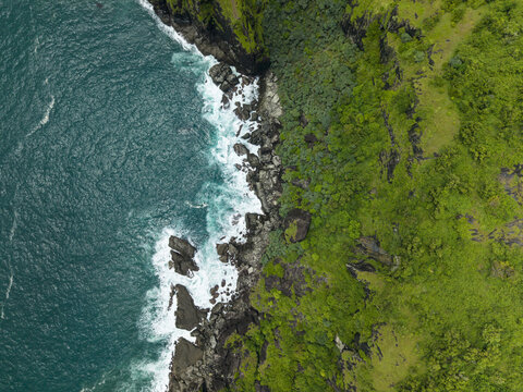 Aerial view of the rugged Pengilon Hill coastline where emerald green cliffs meet the turquoise ocean, Gunungkidul Regency, Daerah Istimewa Yogyakarta, Indonesia.