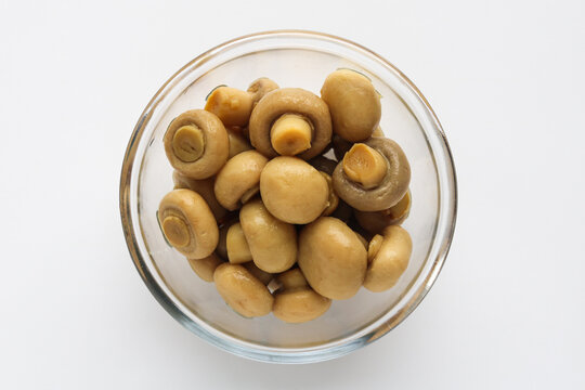 Top view of a clear glass bowl of button mushrooms, isolated on a white background.