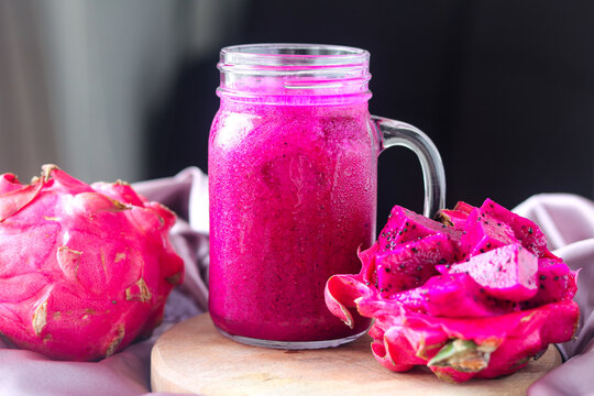 A glass jar of dragon fruit juice with a vibrant pink color, served with fresh fruit pieces.