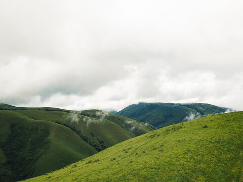 Aerial view of rolling emerald hills disappearing into a soft, misty embrace under a vast, overcast sky, Obudu, Cross River, Nigeria.