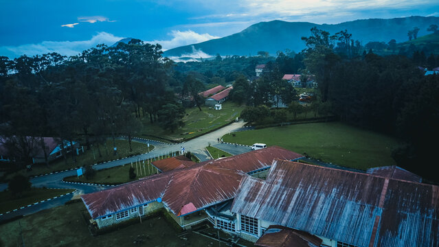 Aerial view of aged reddish roofs amidst vibrant green landscapes and winding roads, under misty mountains and a dramatic sky, Obudu, Cross River, Nigeria.