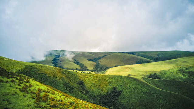 Aerial view of lush emerald slopes and dramatic velvet green hills, partially shrouded in ethereal mist under a dramatic cloudy sky, Obudu, Cross River, Nigeria.