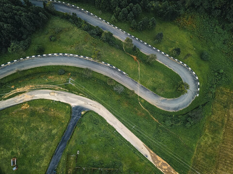 Aerial view of a ribbon of asphalt winding dramatically through vibrant emerald hills and dense, dark green forests, Obudu, Cross River, Nigeria.