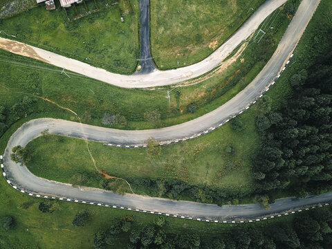 Aerial view of a serpentine asphalt ribbon carving through an emerald landscape, bordered by crisp white barriers and contrasting dark green foliage, Obudu, Cross River, Nigeria.