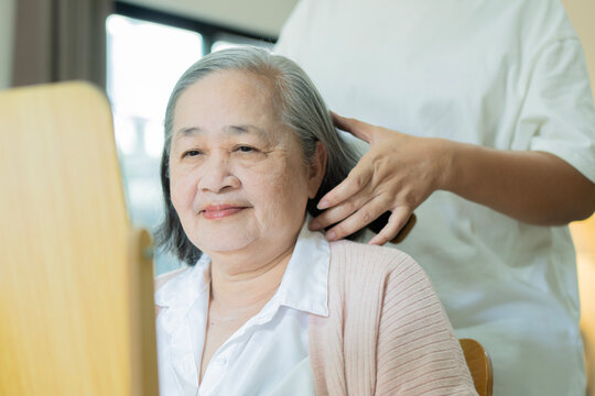 Cheerful senior Asian woman with her daughter is helping her do her hair