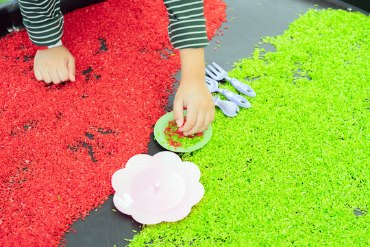 High angle view of a brightly colored red and green dyed wheat seeds with child hands playing