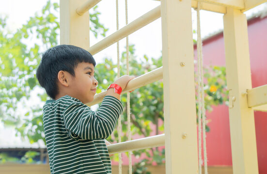 Little boy having fun while climbing on bar at the playground in public park on summer day