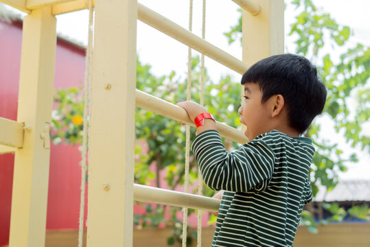 Side view of happy Asian child boy playing and climbing to a steel bar