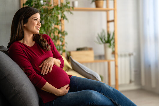 Portrait of young pregnant woman holding hands on her belly at modern home. Pregnancy, motherhood