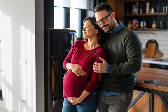 Overjoyed pregnant wife hugging husband enjoying romantic moments at home during the last trimester.