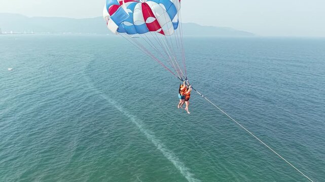 Two people parasailing high above the blue sea, enjoying an exhilarating summer extreme sport, experiencing freedom, adventure, and excitement during tropical beach vacation outdoor activity