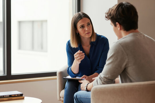 Female therapist talks to teenage boy in office about his problems. Woman listens attentively, offers support and guidance. Teenager looks troubled, seeking help. Professional mental health session.