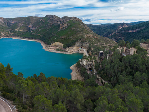 Aerial panoramic view of Benageber dam and turquoise reservoir on the Turia River surrounded by green pine forests and rocky mountains in Valencia, Spain