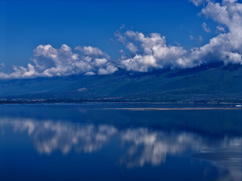 Aerial view of Lake Kerkini with white clouds reflecting on the calm blue water surface and mountains in the background Serres, Greece.