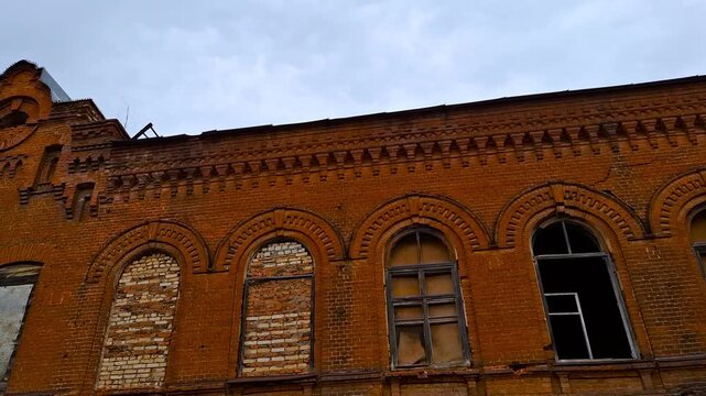 Abandoned tobacco factory building in Yelets, late 19th century. Historic red brick industrial architecture with arched windows and urban decay textures under a cloudy sky.