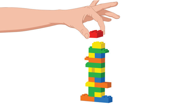 A human hand carefully places a small red plastic brick onto a tall colorful tower constructed from miscellaneous interlocking construction toy building blocks.