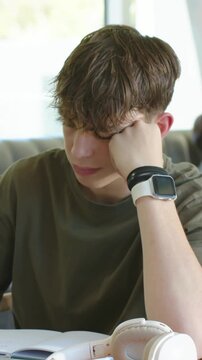 Vertical video: Leaning, youth reading over open book in bright room with headphones and watch