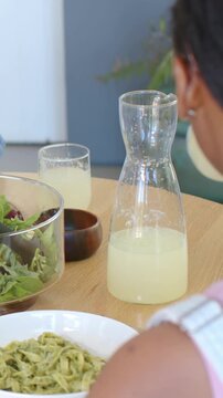 Vertical video: Camera shifting mom serving salad while girl in pink holding glass at home, carafe