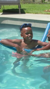 Vertical video: Placing hands dad guiding son learning in home pool with noodle goggles pink trunks