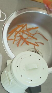 Vertical video: Entering hands in yellow tee and watch collecting carrot peels at sink for compost