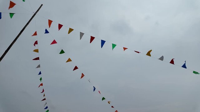 Colorful Triangular Flags Flutter Against Cloudy Sky, Creating Bright and Festive Outdoor Celebration with Vibrant Decorations and Joyful Atmosphere.