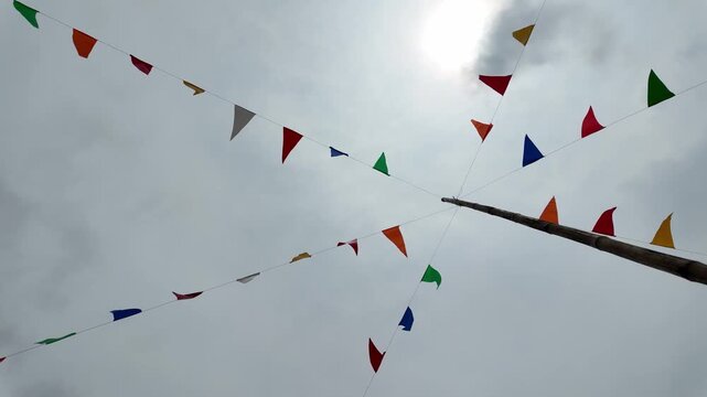 Colorful flags fluttering in bright outdoor sky, adorned with clouds, create festive atmosphere of celebration and joy, making every party vibrant and memorable.