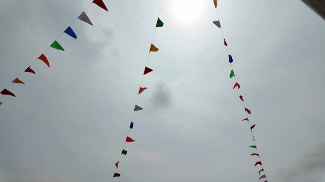 Brightly colored flags flutter against cloudy sky, creating festive atmosphere that enhances outdoor celebration with vibrant hues and joyful decoration, perfect for summer.