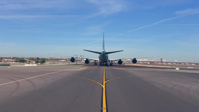 Immersive cockpit view taken from inside a jet taxiing behind a massive 4-engine jet taxiing through M;adrid airport, with the Terminal 4 and Madrid skyline at the background. Early morning light.