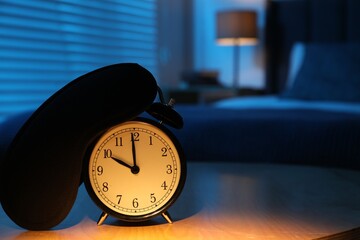 Naklejka premium Alarm clock and sleeping mask on table in bedroom at night, closeup. Space for text