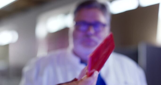 Two people in a workshop holding and examining a curved red aerodynamic car part under bright lighting