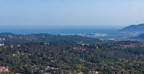 Fototapeta premium Aerial view of Grasse, pine covered hills and wooded slopes descend to the Mediterranean and the Cote d'Azur, curved bay and headlands sit under clear midday light.